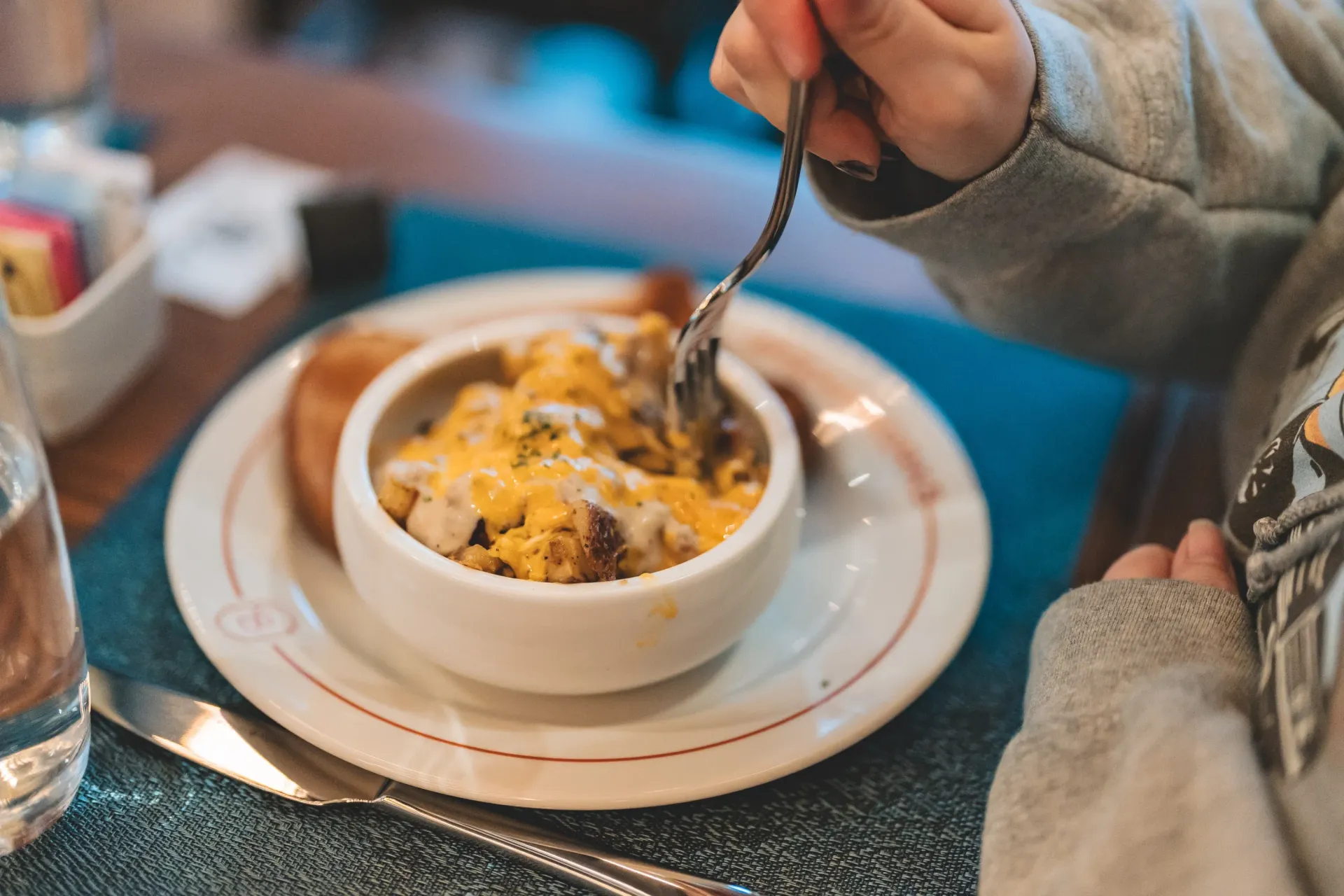 Person eating a bowl of food, topped with cheese, with a fork at a table.