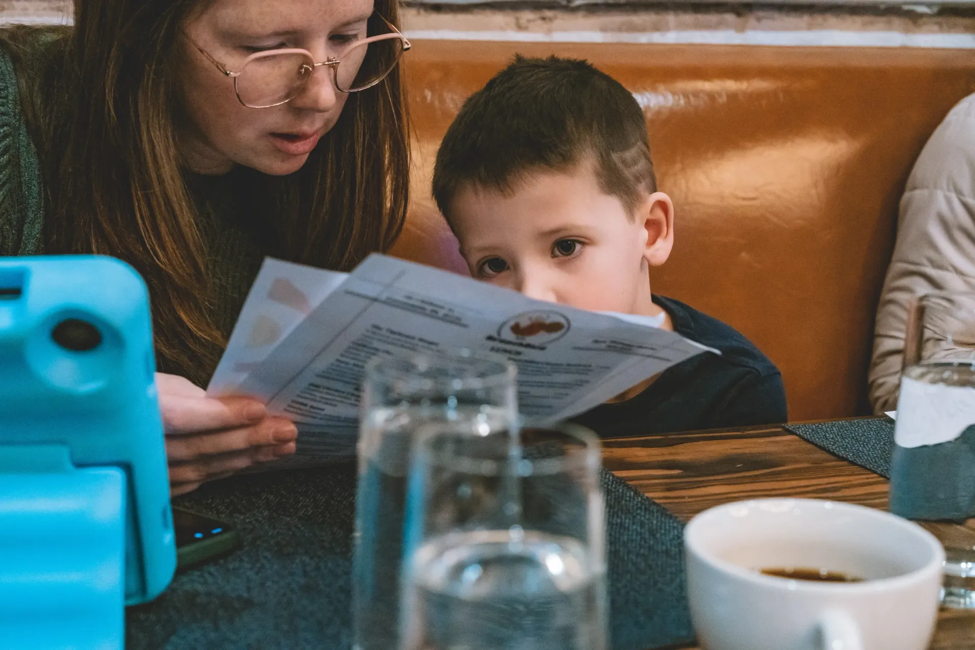 Woman and child looking at a menu in a restaurant. The child appears focused, looking down at the menu.