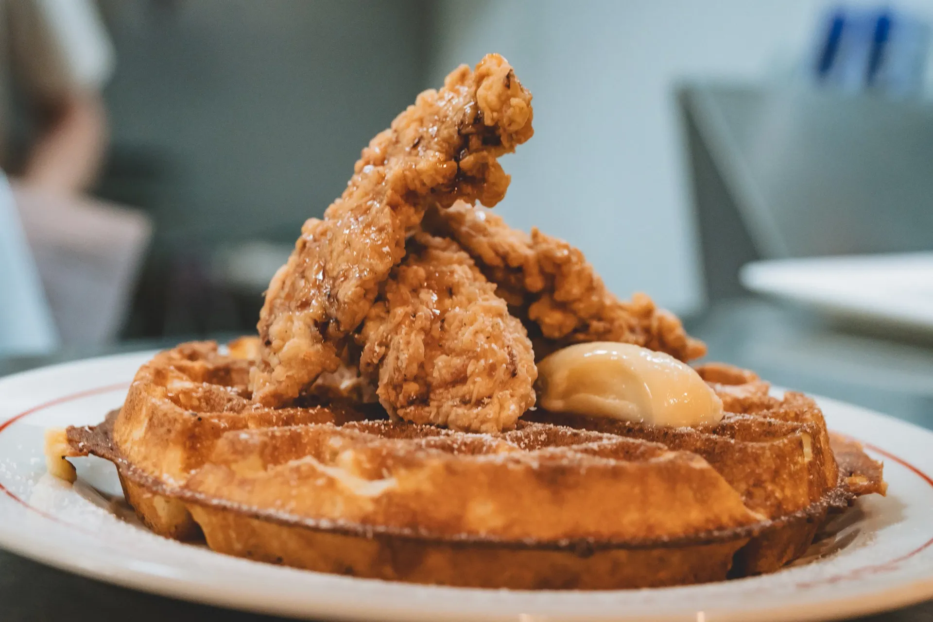 Chicken and waffles: golden-brown waffle with fried chicken and butter on a white plate.