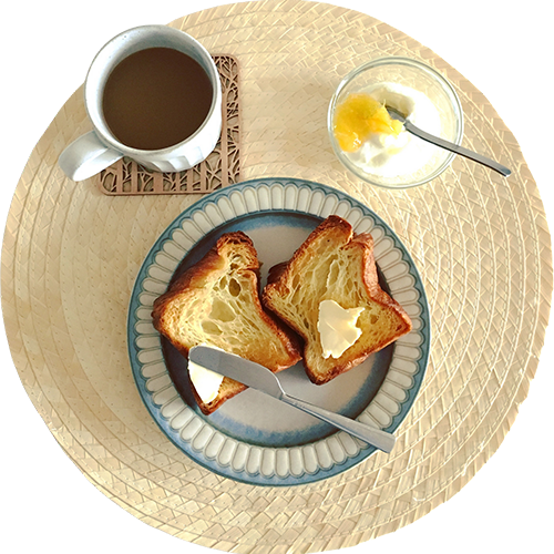 Breakfast: buttered toast, coffee, yogurt with fruit on a round placemat.