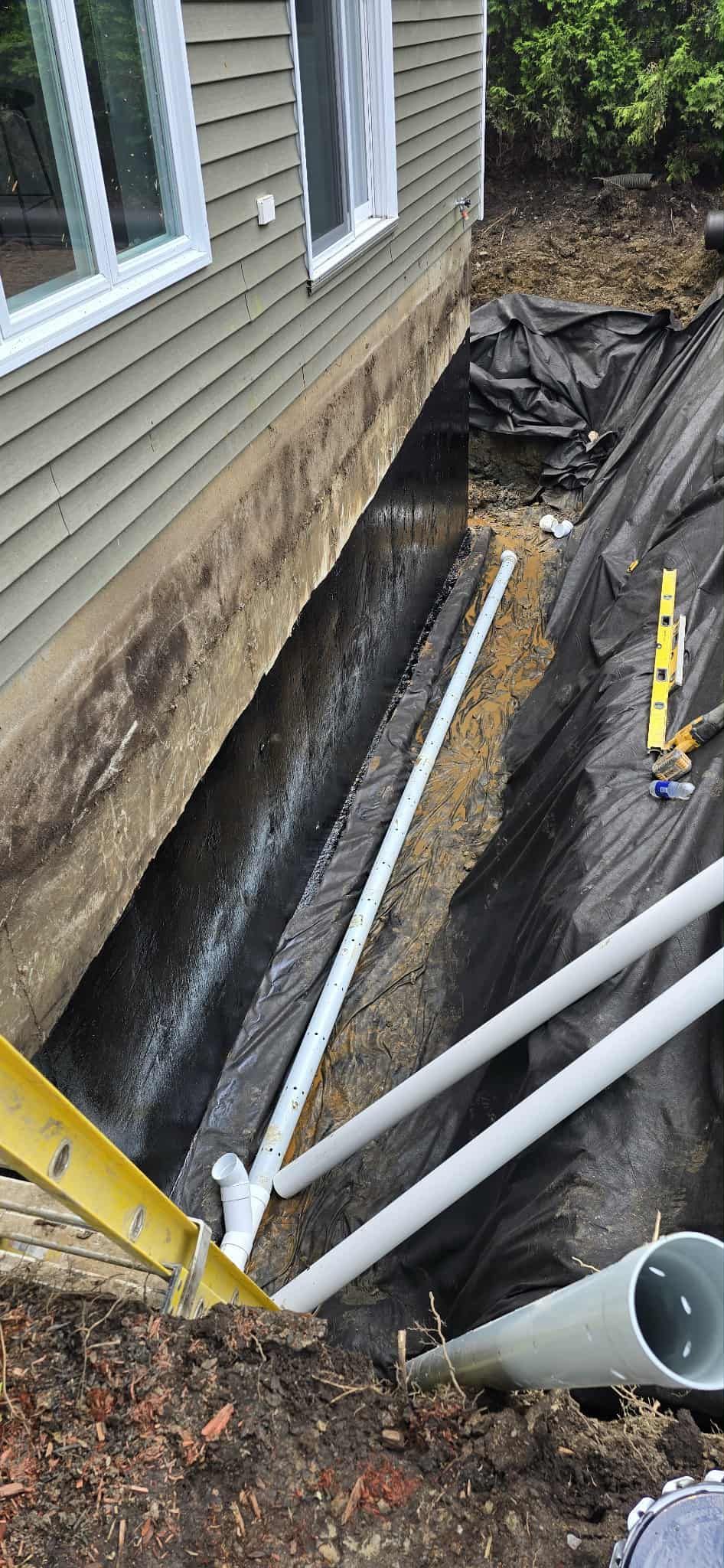 Tranchée extérieure de la maison avec tuyaux blancs pour le drainage.