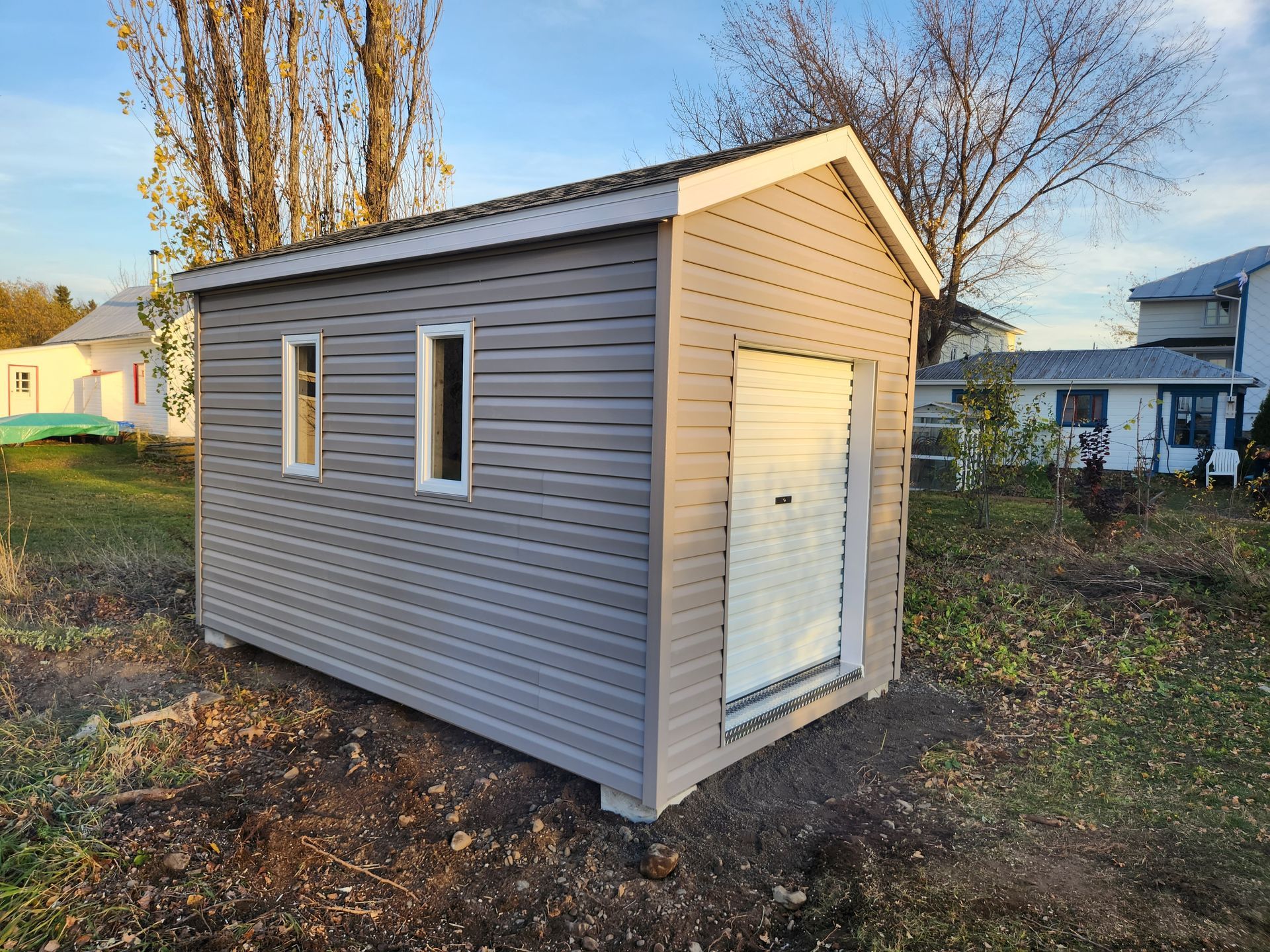 Un petit hangar se trouve au milieu d'un champ devant une maison.