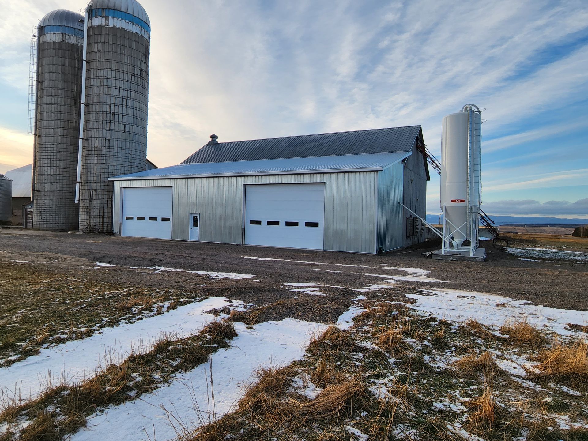 Une grange avec deux silos en arrière-plan dans un champ enneigé.