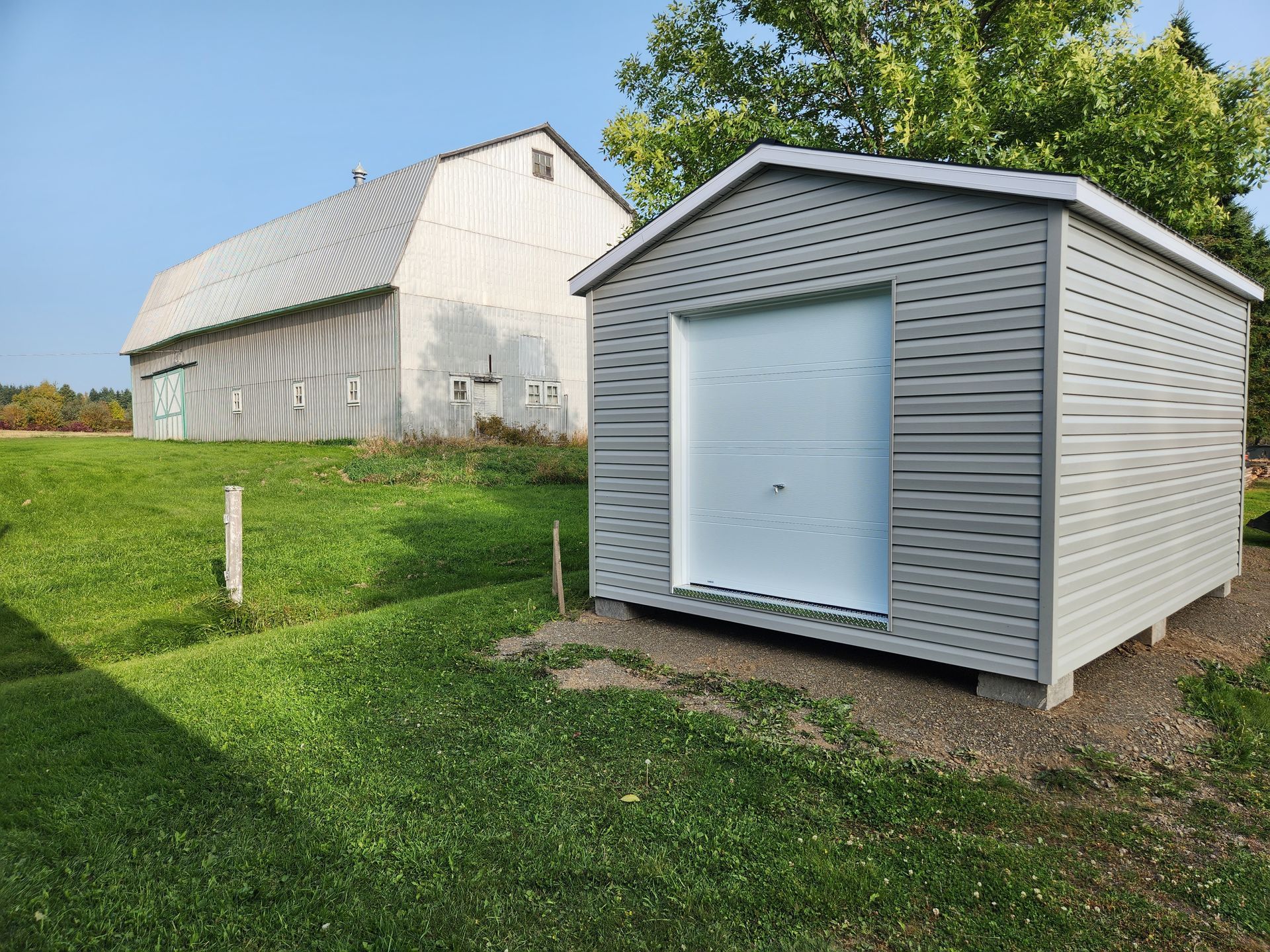 Un hangar avec une porte de garage est assis dans l'herbe à côté d'une grange.