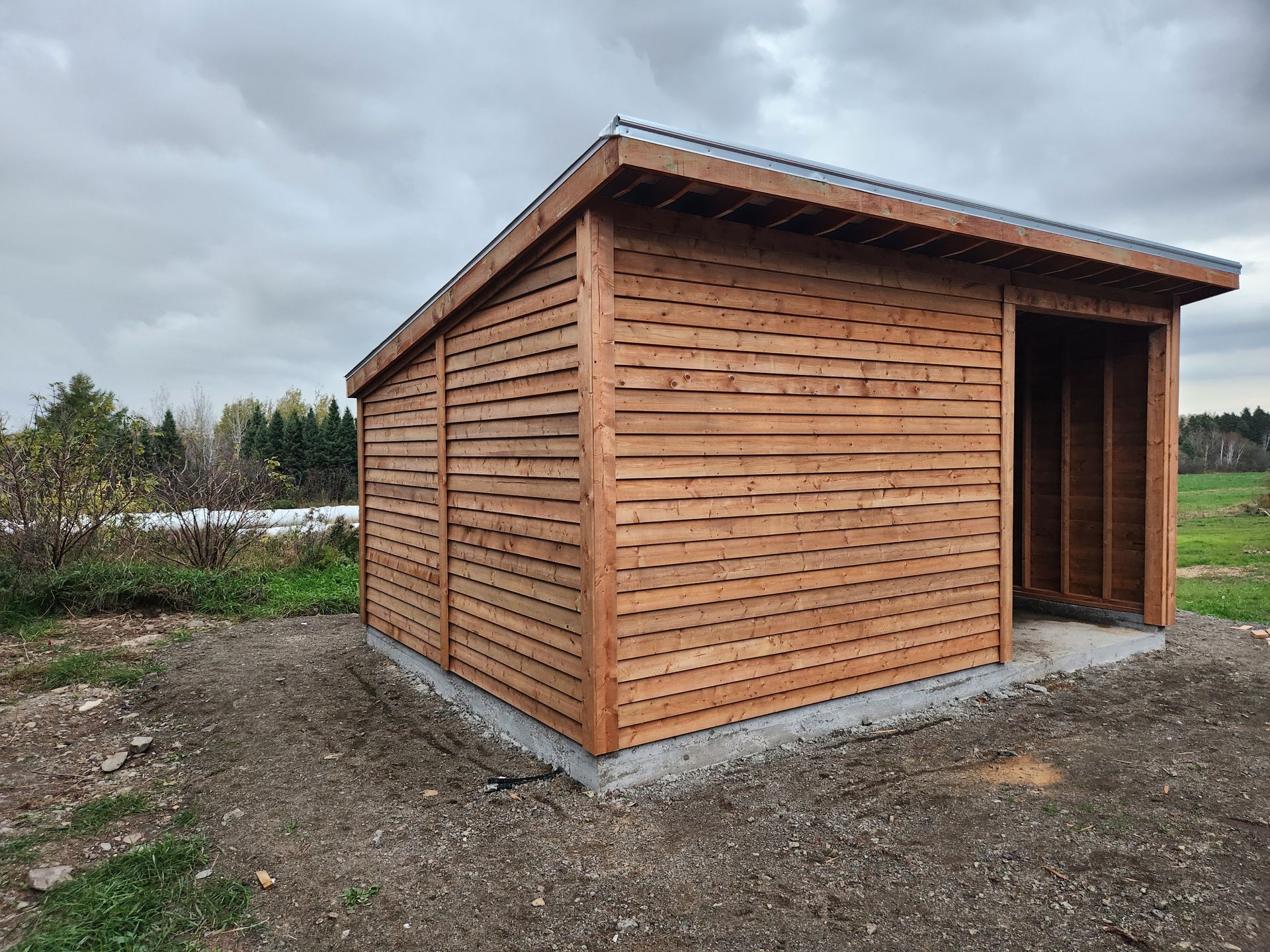 Un petit hangar en bois se trouve au milieu d'un champ de terre.
