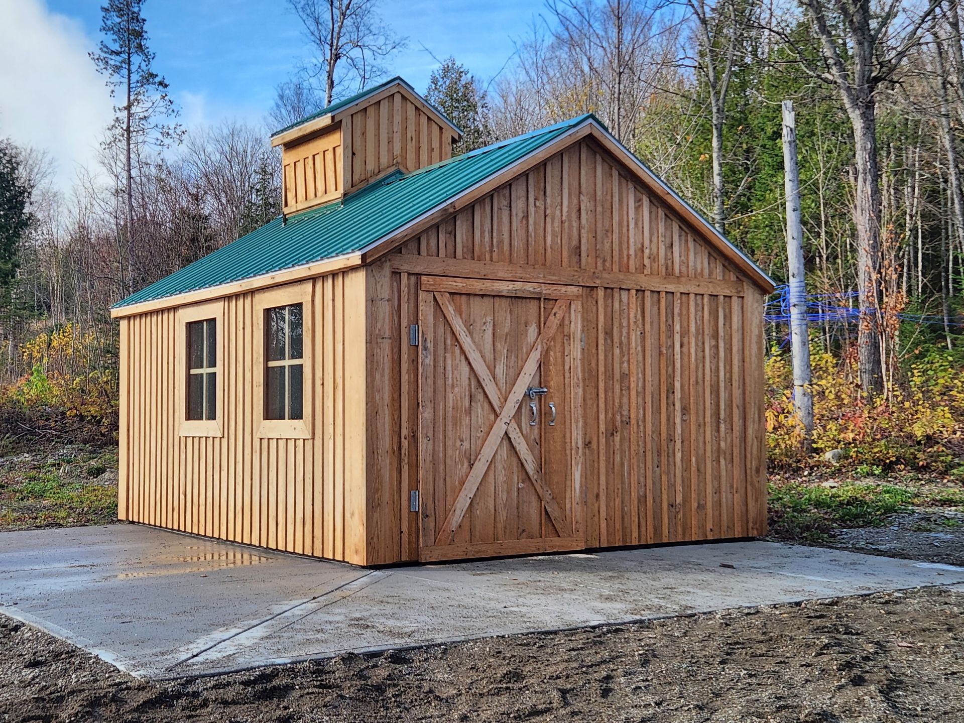 Un hangar en bois avec un toit vert se trouve au milieu d'une forêt.