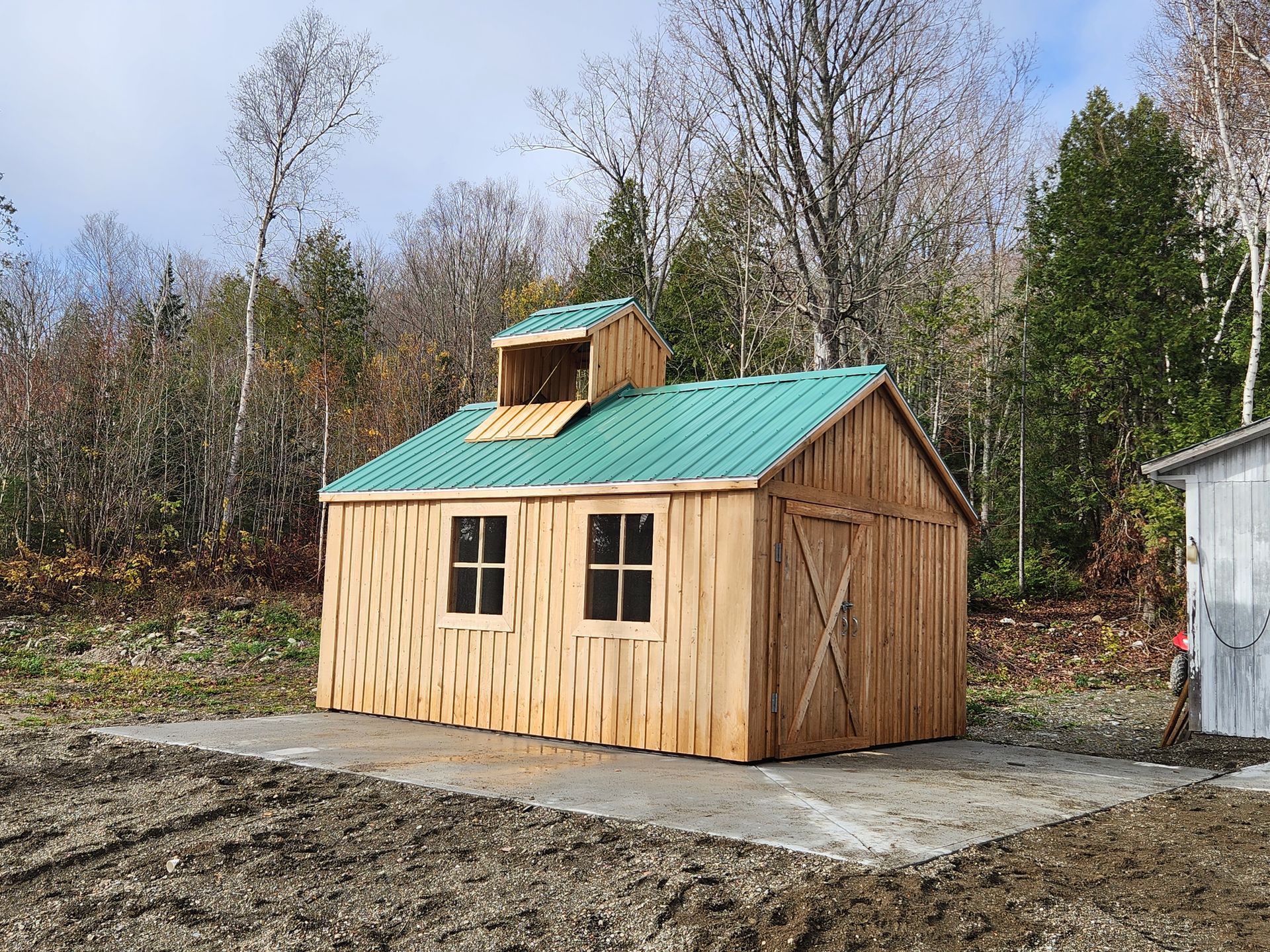 Un hangar en bois avec un toit vert se trouve au milieu d'un champ de terre.
