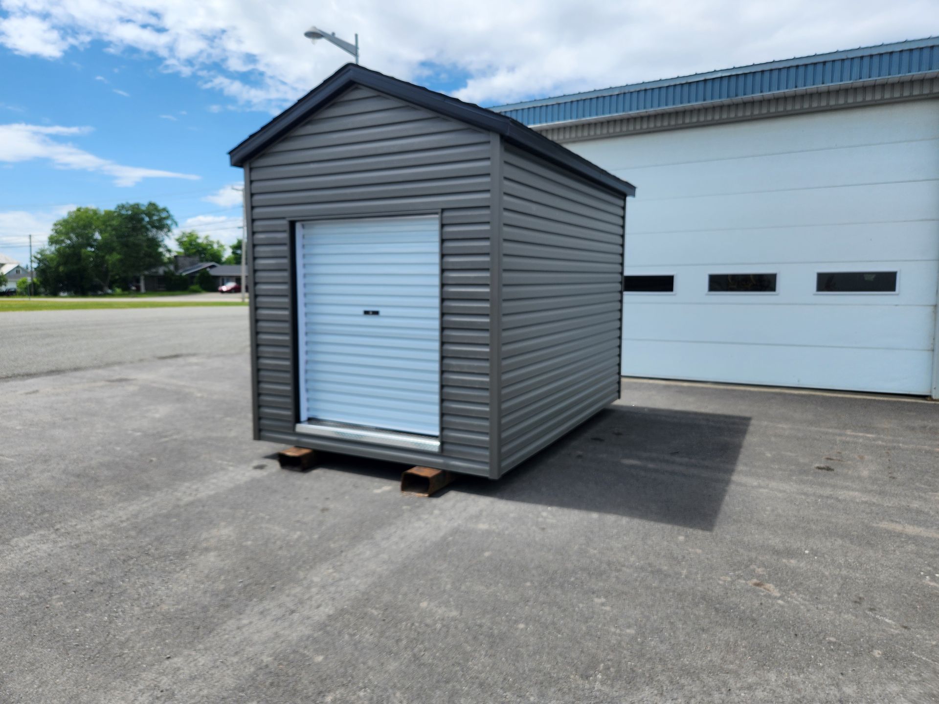 Un petit hangar avec une porte blanche se trouve devant une porte de garage.