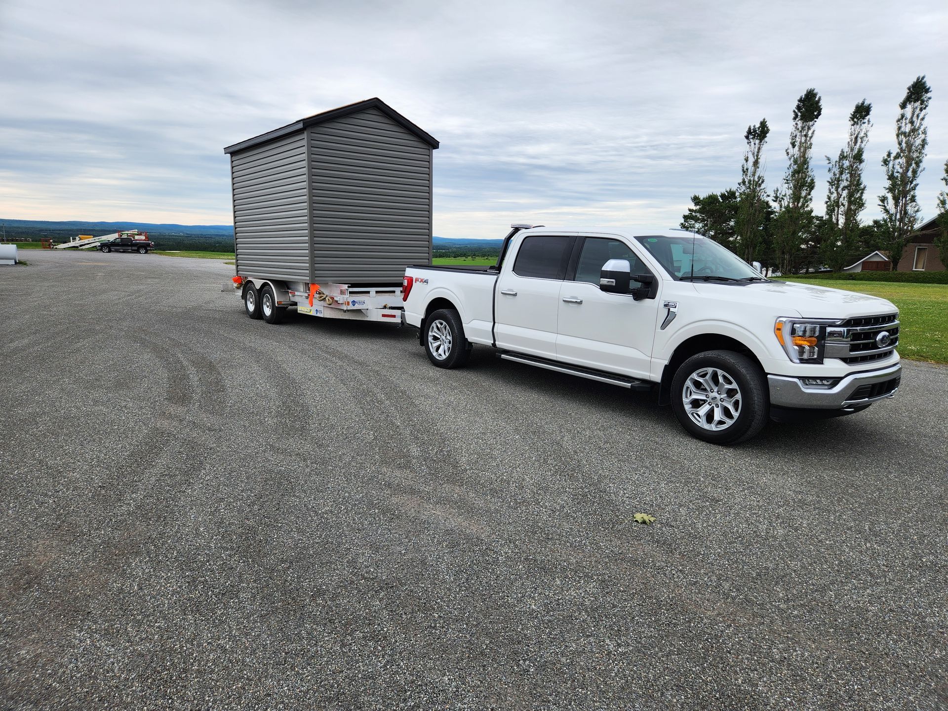 Un camion blanc remorque un petit hangar sur une remorque.