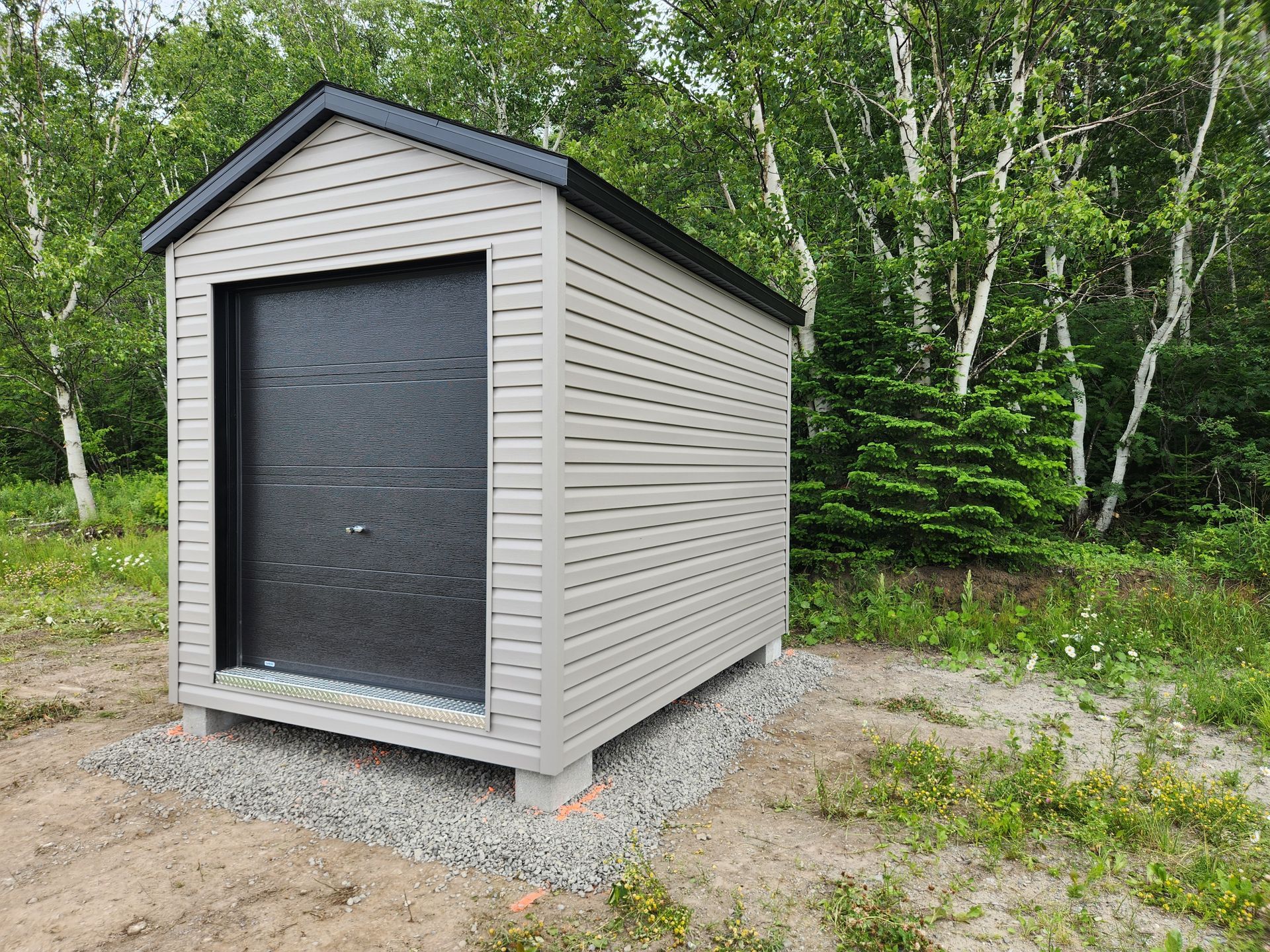 Un petit hangar avec une porte noire se trouve au milieu d'un champ.