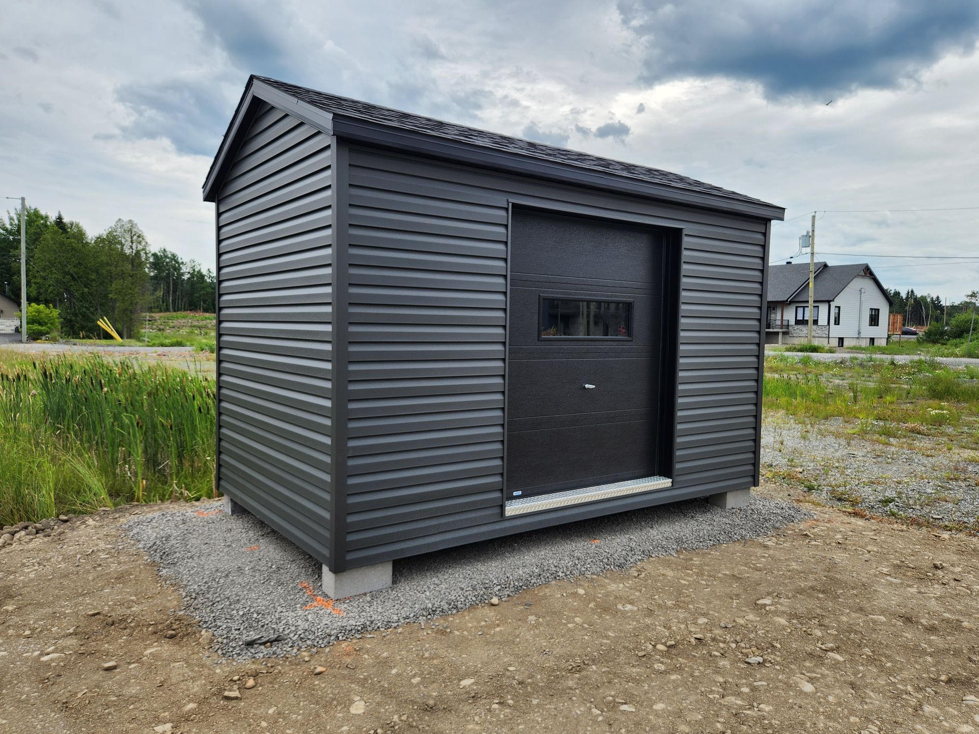 Un hangar noir avec une porte de garage se trouve au milieu d'un champ de terre.