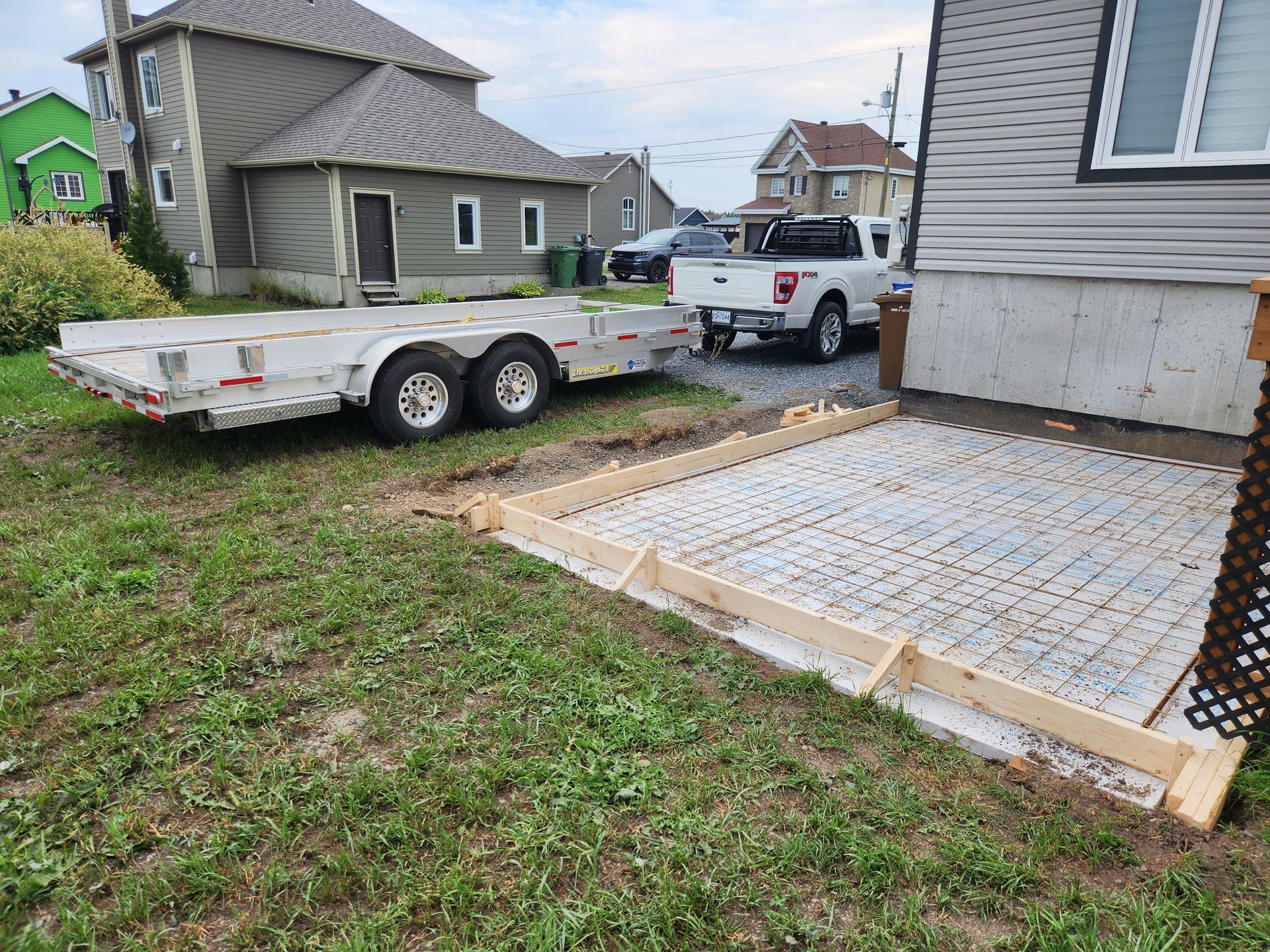 Un camion blanc est garé à côté d'une remorque devant une maison.