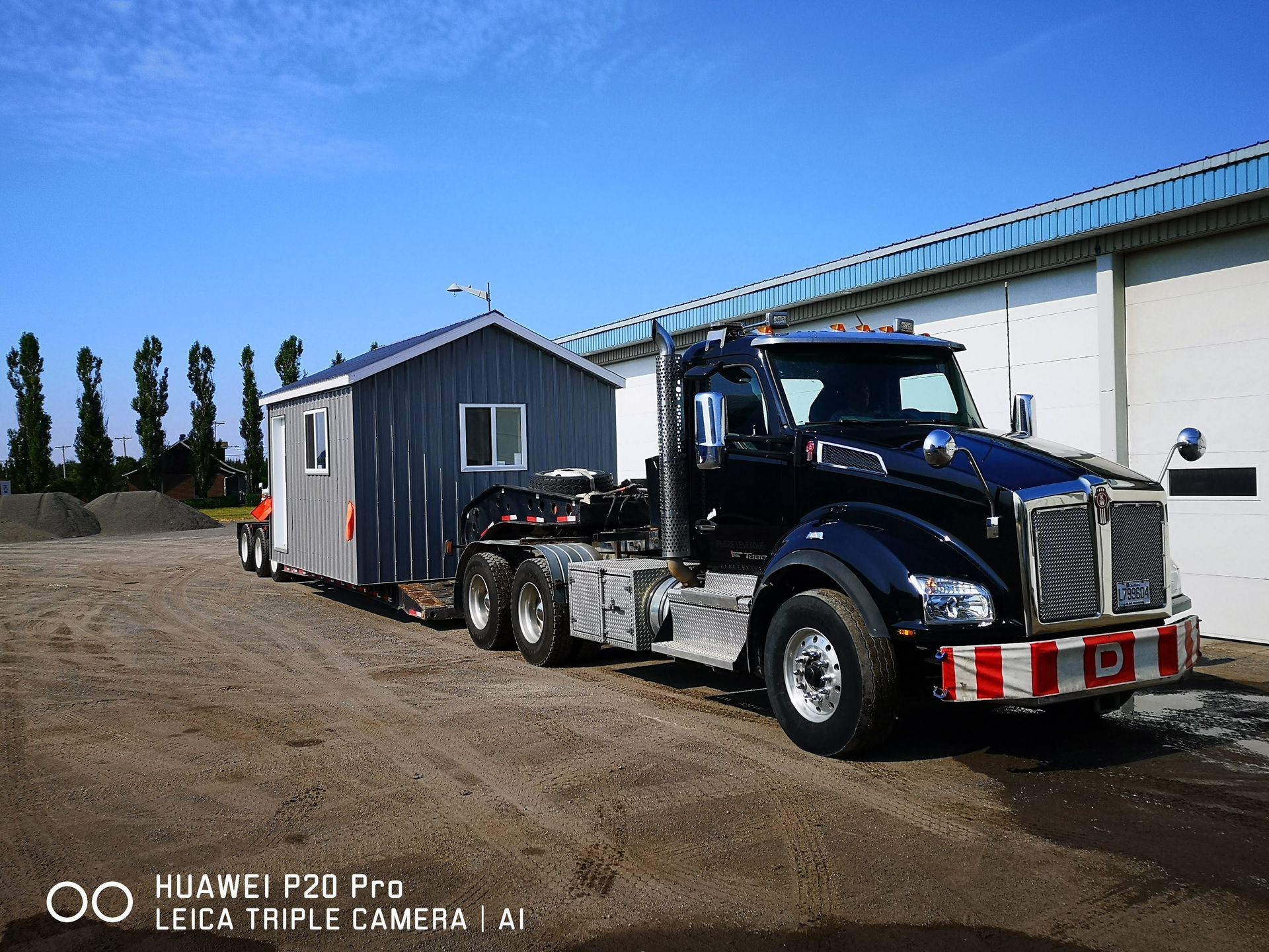 Un semi-remorque noir tire une remorque devant un bâtiment.