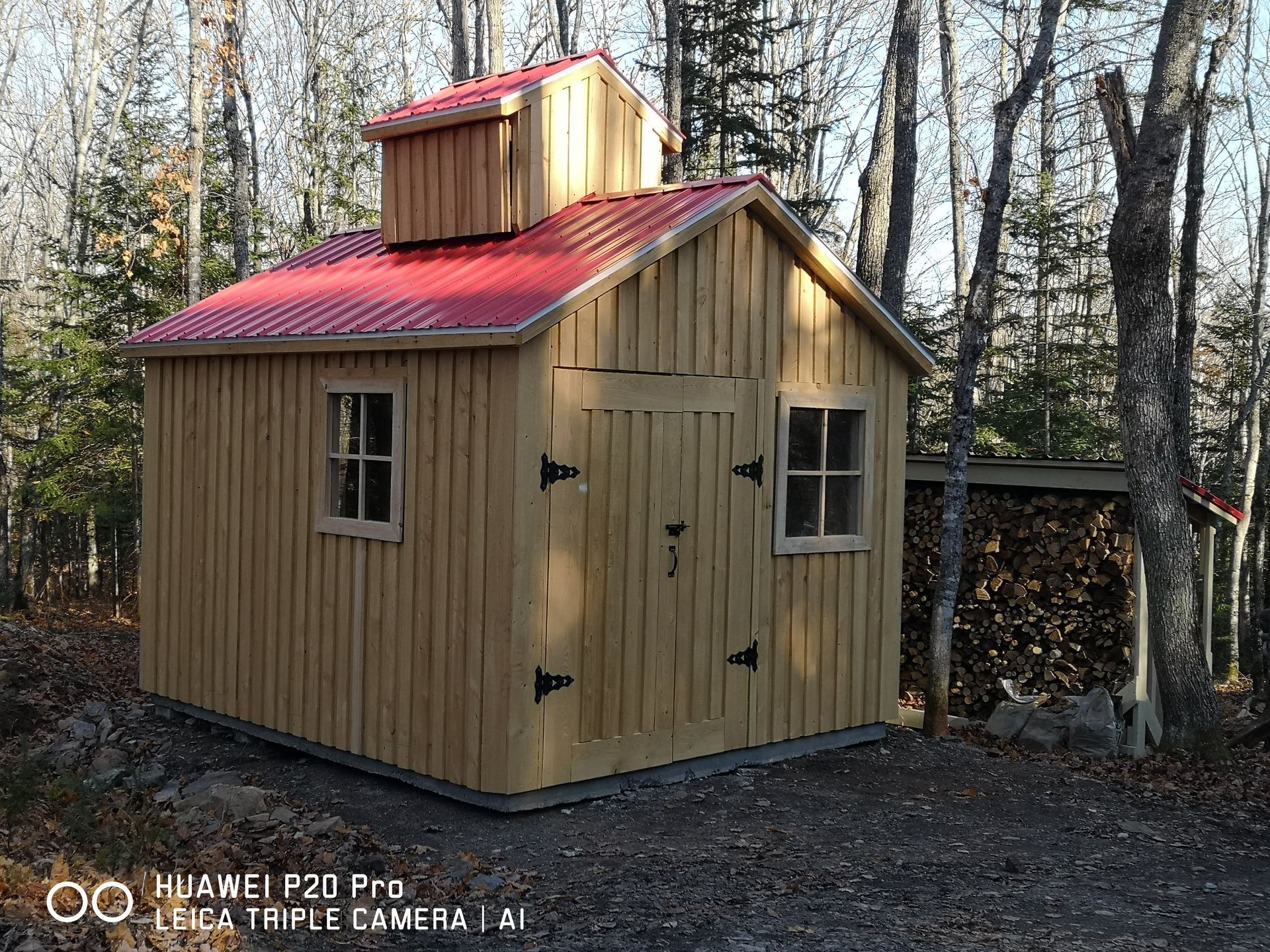 Un hangar en bois avec un toit rouge au milieu d'une forêt.