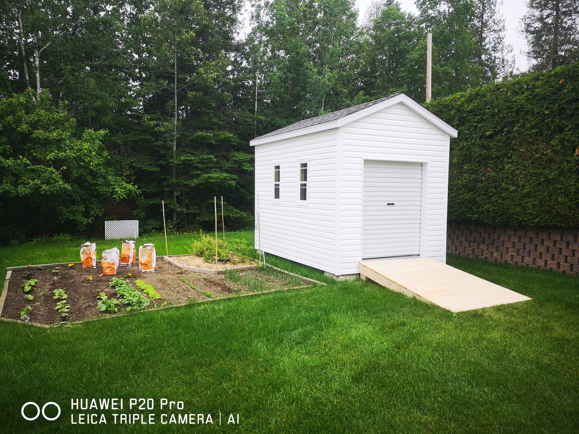 Un hangar blanc se trouve au milieu d'une cour verdoyante à côté d'un jardin.