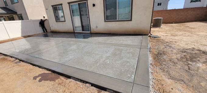 A concrete patio is being built in the backyard of a house.