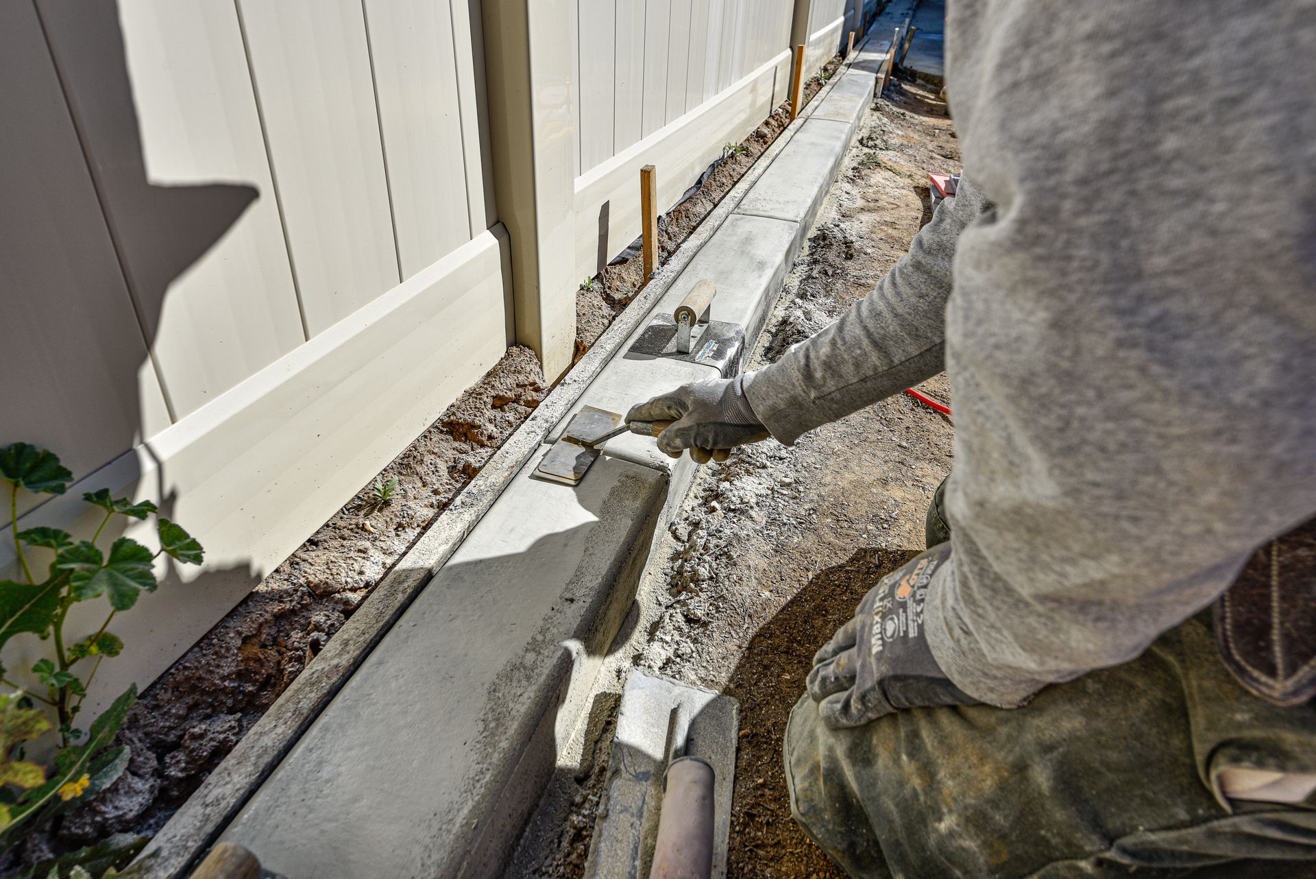 A man is kneeling down and working on a sidewalk next to a fence in Beaumont, CA.