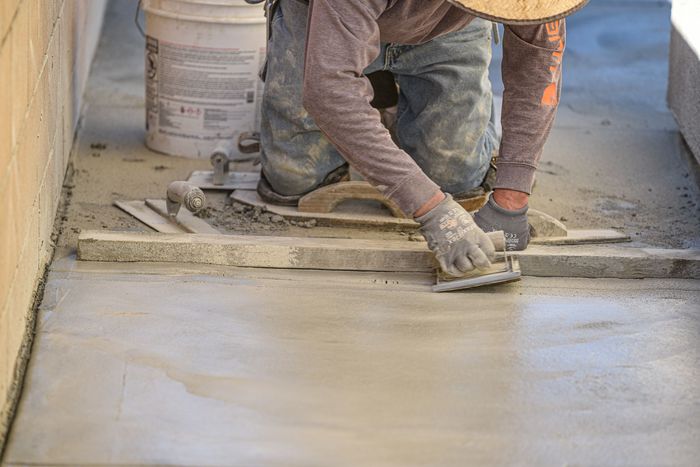 A man is kneeling down and spreading concrete on a sidewalk in Beaumont, CA.