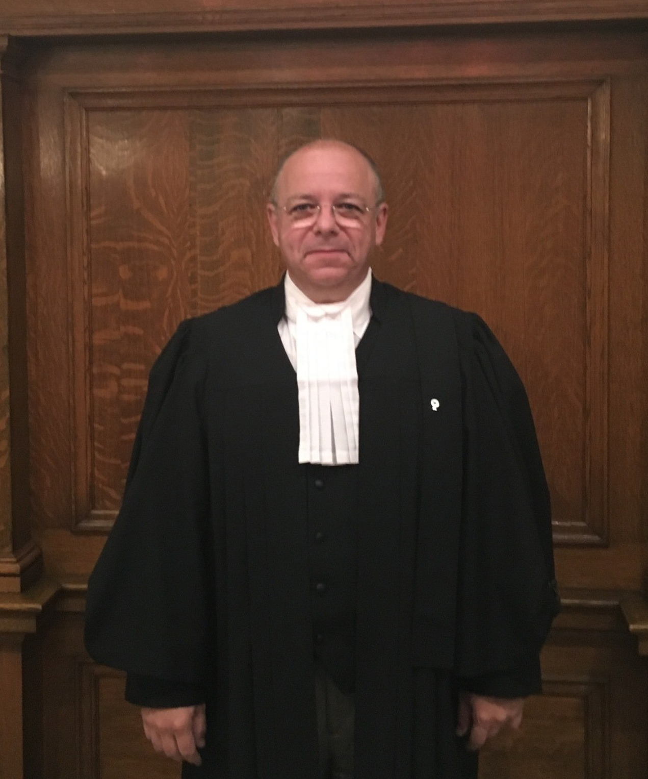 Un homme vêtu d’une robe noire se tient devant un mur en bois.