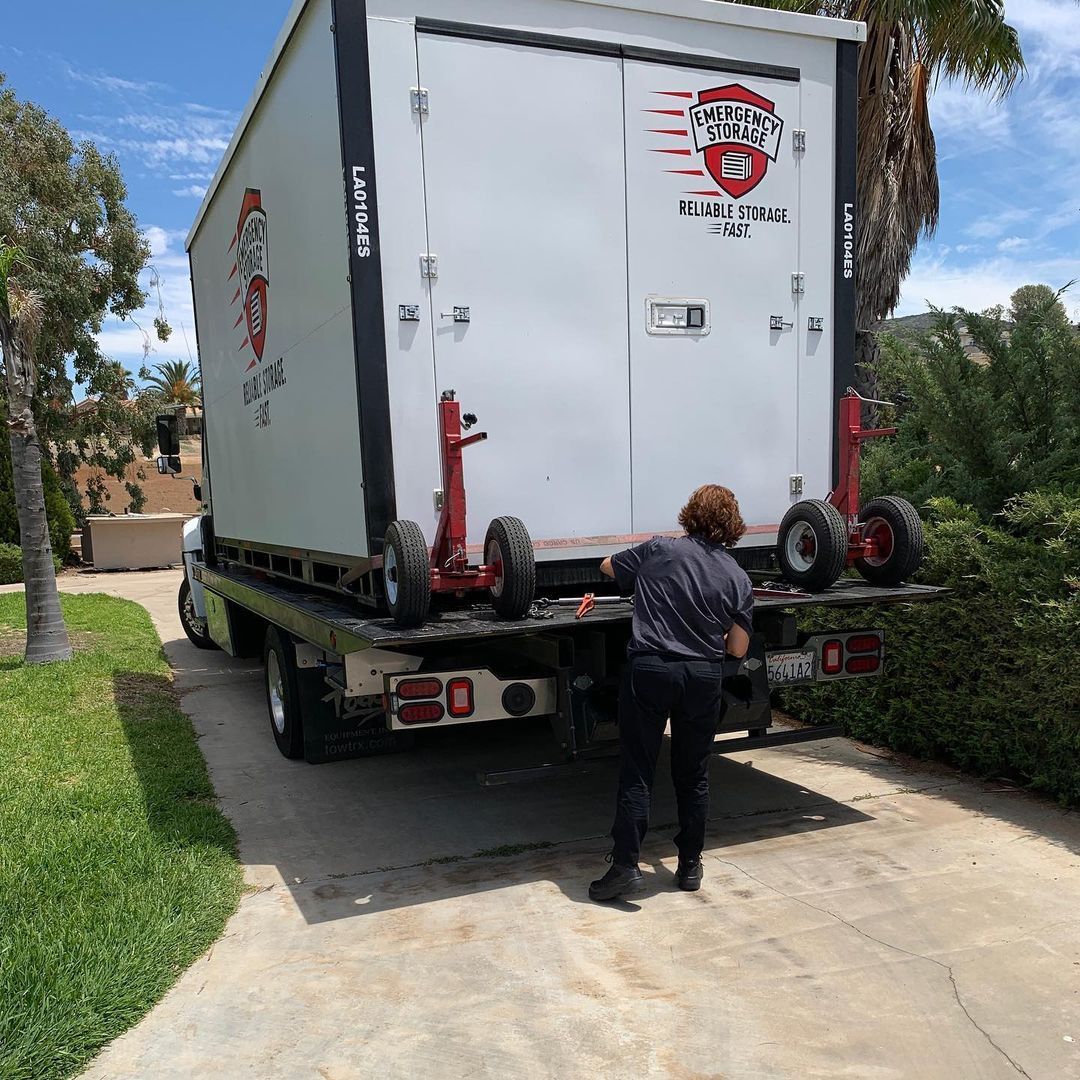 A woman is standing next to a storage container truck in a driveway.