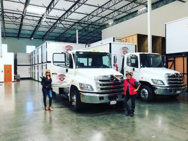 2 women standing next to emergency storage delivery trucks