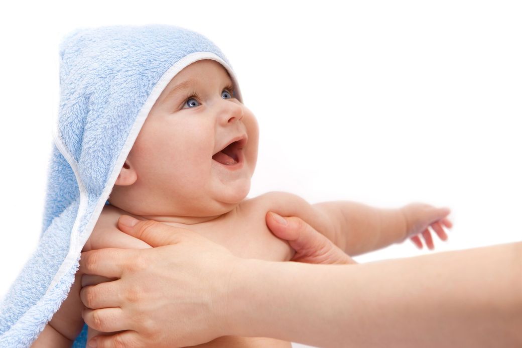 Un bambino avvolto in un asciugamano blu, tenuto in braccio, sorride e guarda in alto con la bocca aperta.