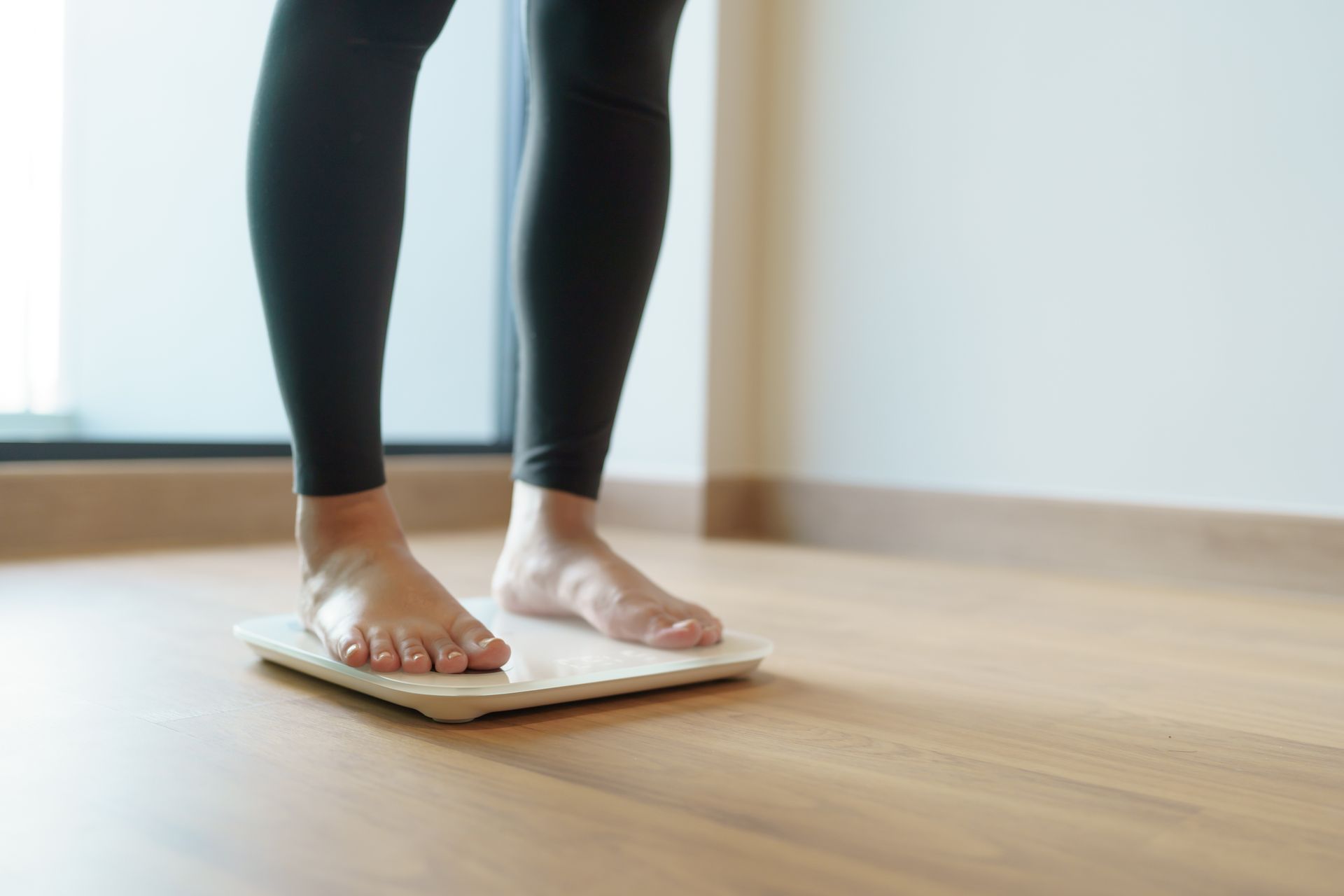 A woman is standing on a scale on a wooden floor.