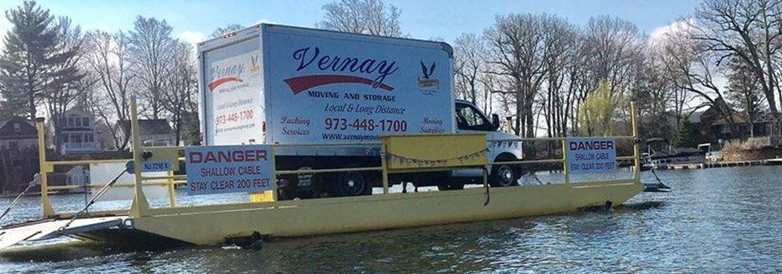 A branded Vernay Moving and Storage box truck crossing a lake on a barge during a long distance job