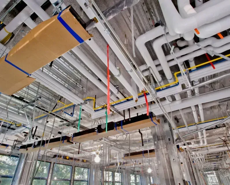 A building under construction with a lot of pipes hanging from the ceiling.