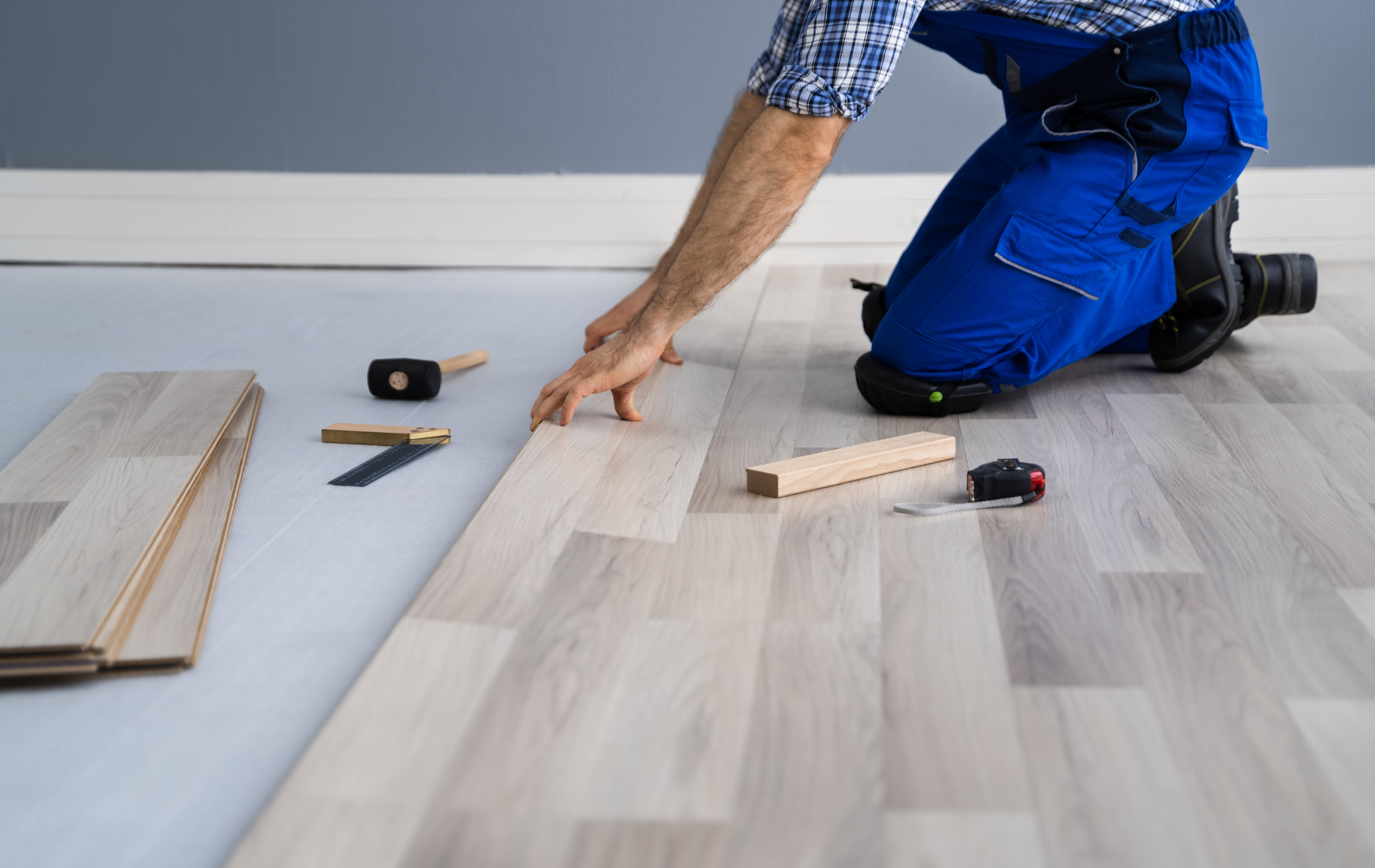 A man is kneeling down to install a wooden floor.