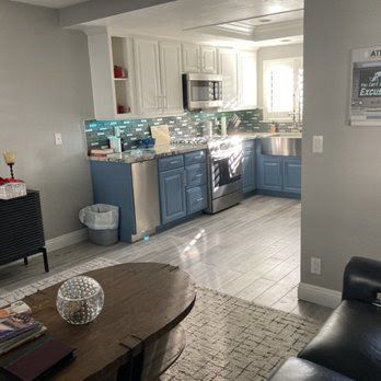 A living room filled with furniture and a kitchen with blue cabinets and stainless steel appliances.
