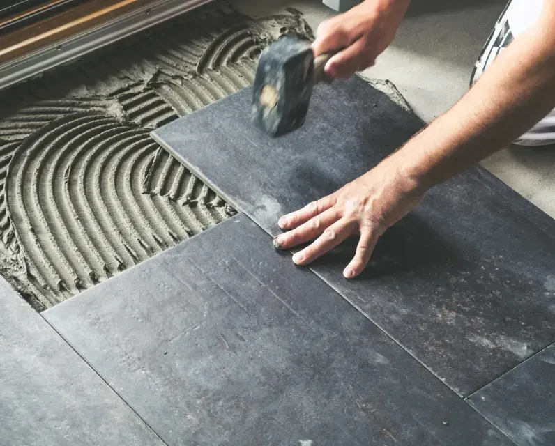 A person is laying tiles on the floor with a hammer.
