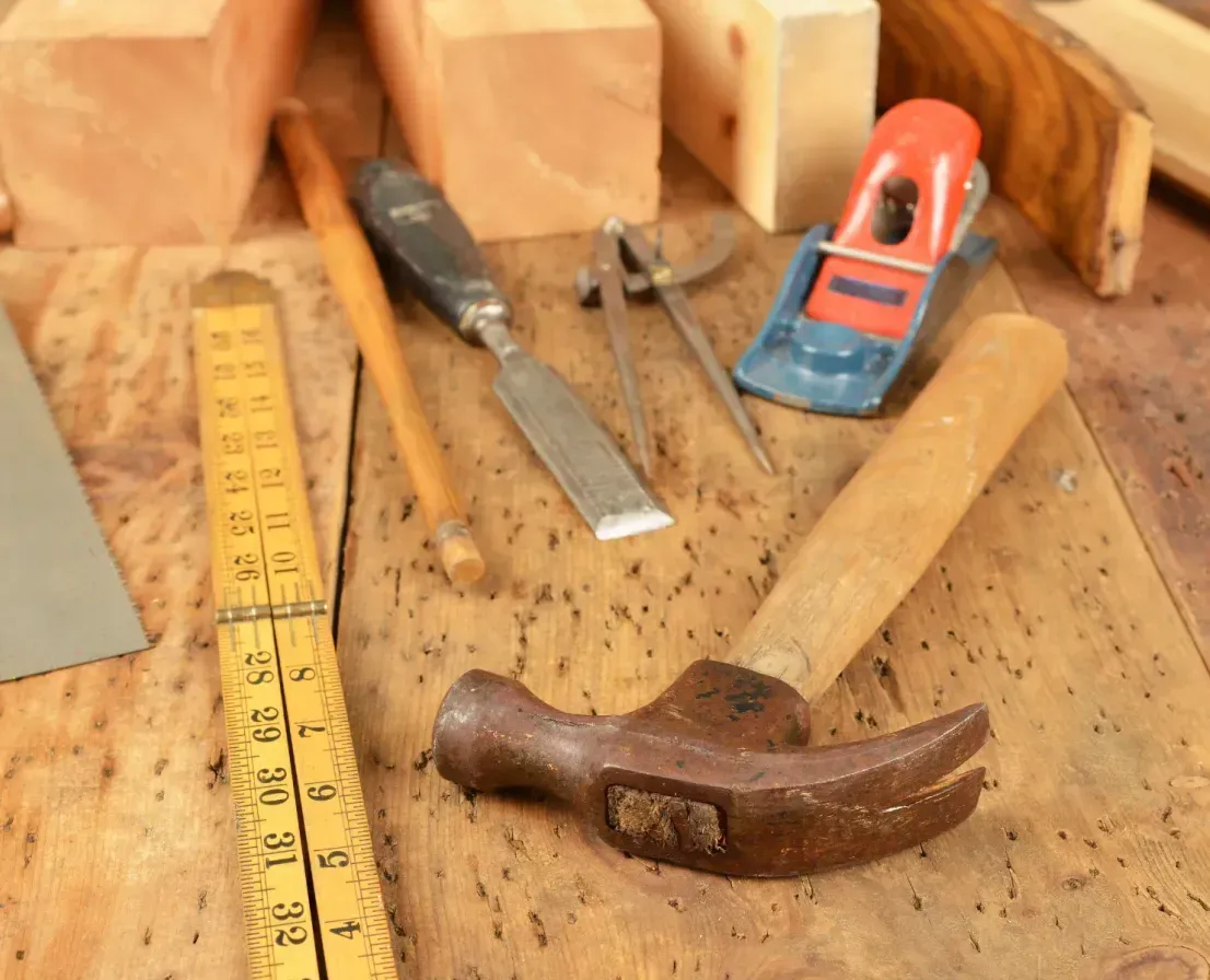 A hammer is sitting on a wooden table with other tools