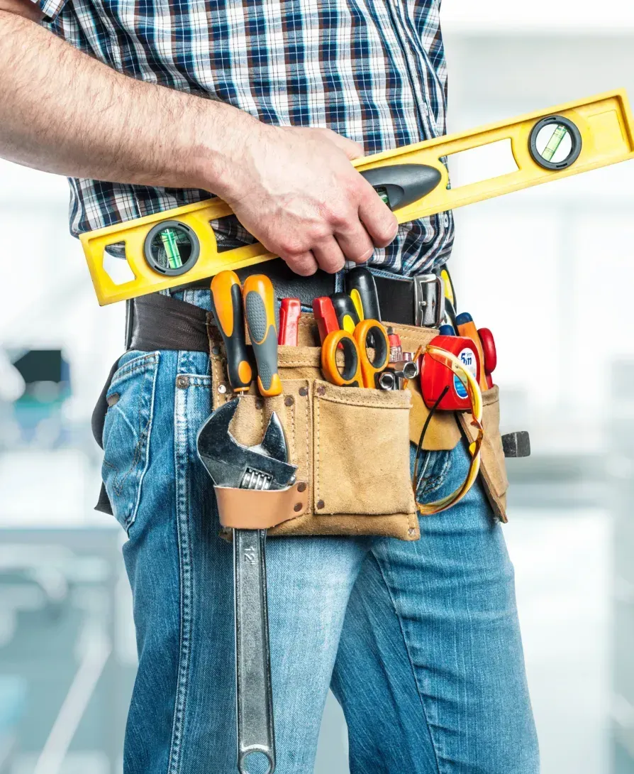 A man wearing a tool belt is holding a level.