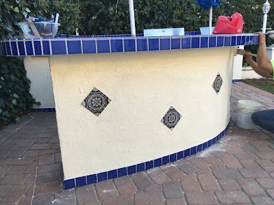 A man is painting a curved table with blue tiles.