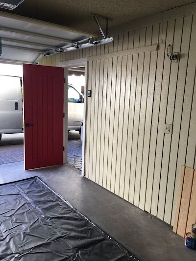 A red door is open in a garage with a van parked in the background.