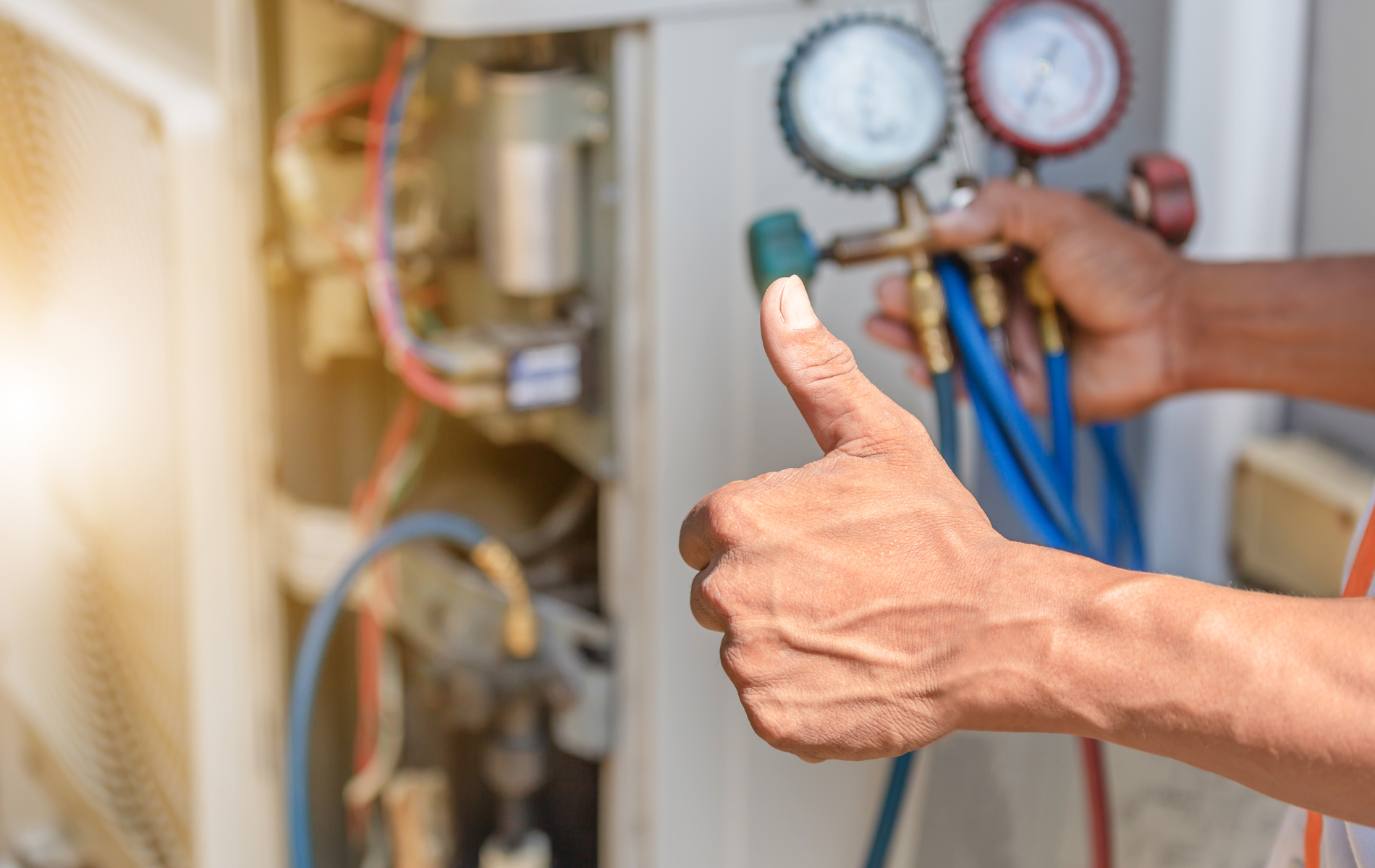 A man is giving a thumbs up while working on an air conditioner.