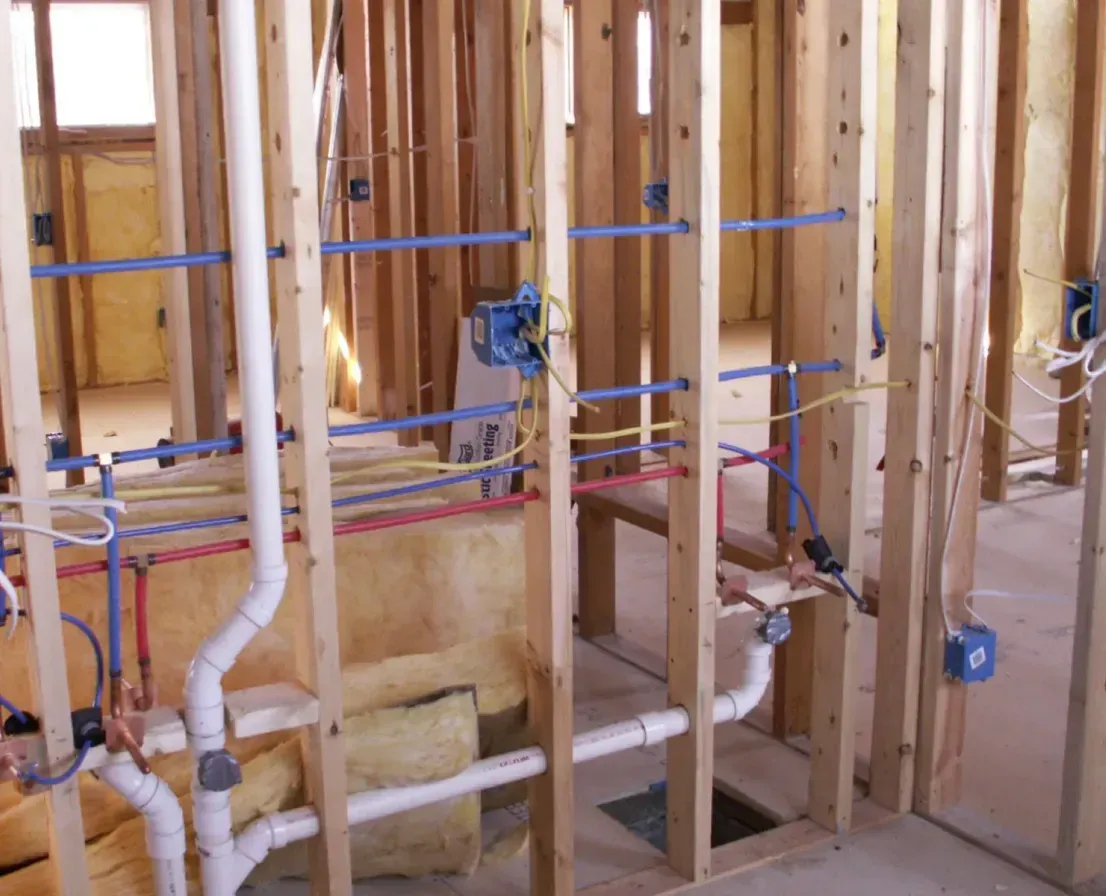 A room in a house under construction with pipes and wires.