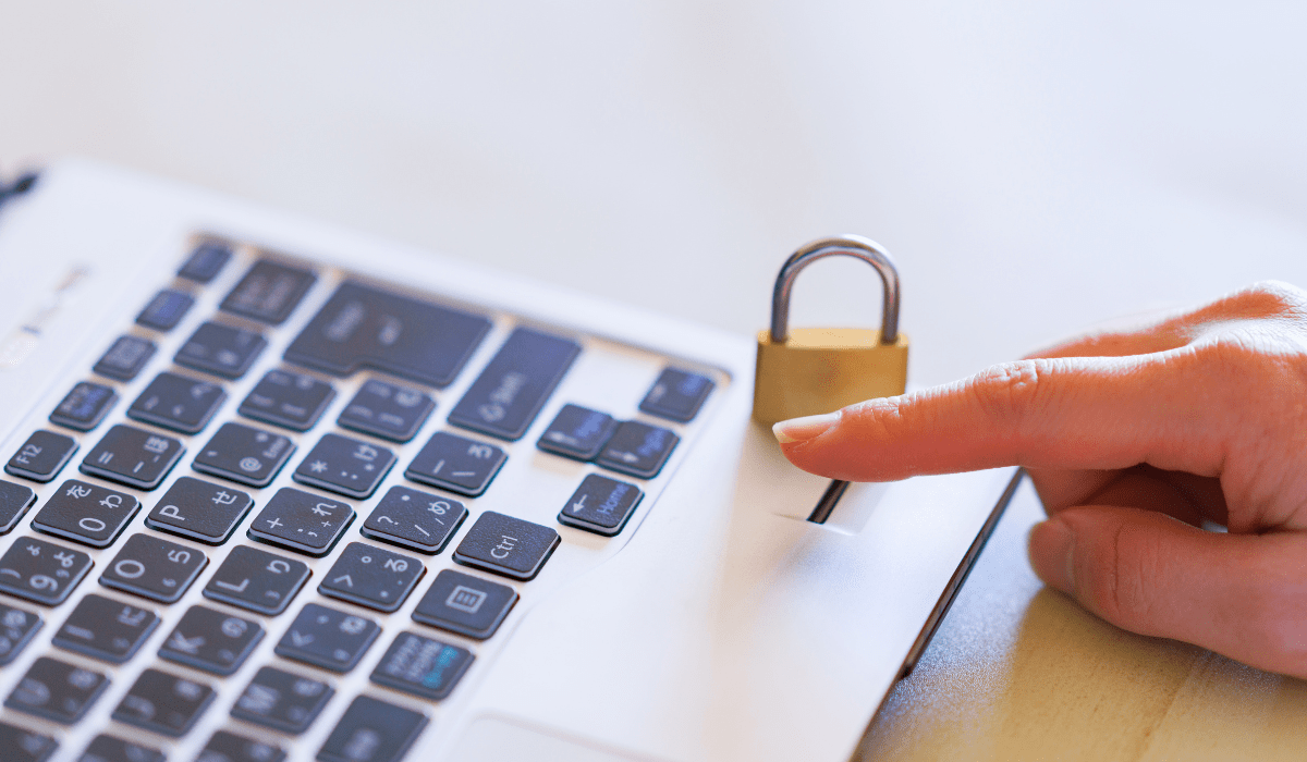 Uma pessoa está segurando um cadeado sobre o teclado de um laptop.