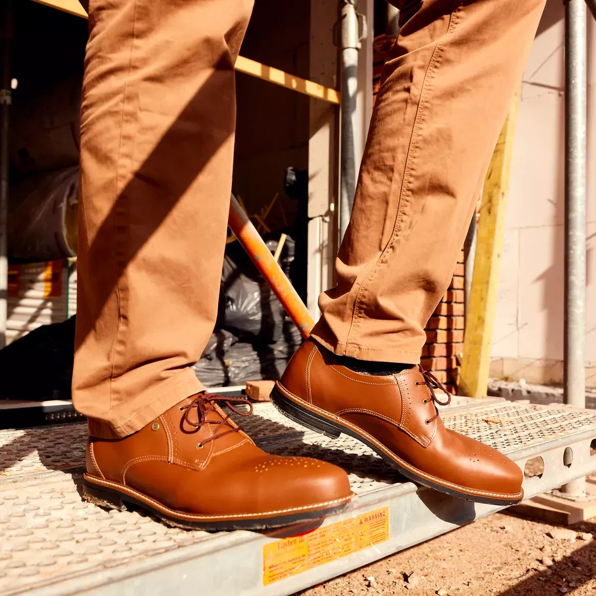 Man wearing brown shoes and pants standing on a metal platform at a construction site.
