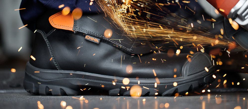 A person wearing a pair of black safety boots is grinding a piece of metal.