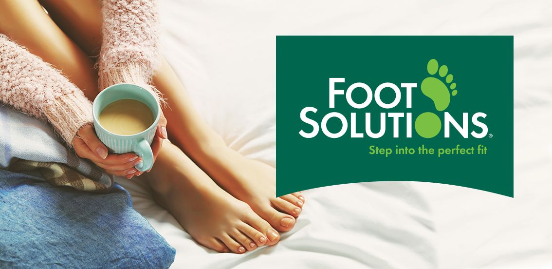 Woman relaxing in bed with a cup of coffee, feet in focus next to a