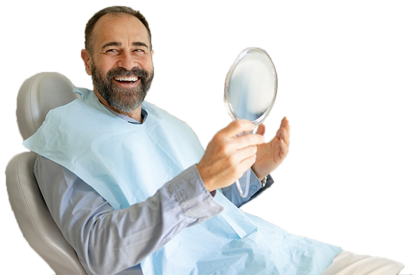 A man is sitting in a dental chair looking at his teeth in a mirror.