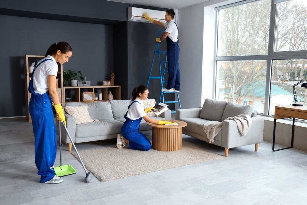 Four cleaning professionals in blue jumpsuits cleaning a living room.