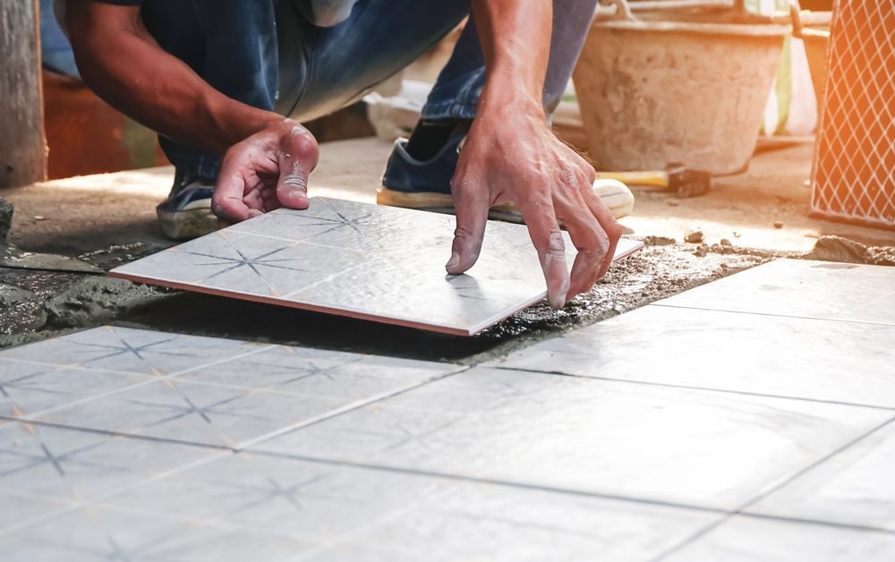 Person installing a ceramic tile floor; hands placing tile on mortar.