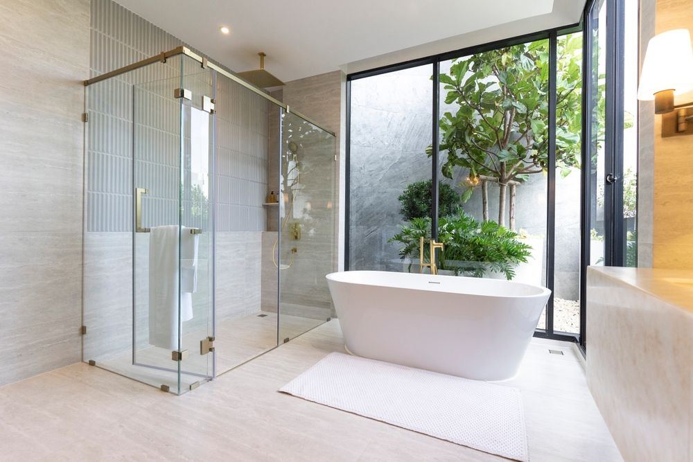 Spacious modern bathroom with a freestanding tub, glass shower, and a view of a small garden.