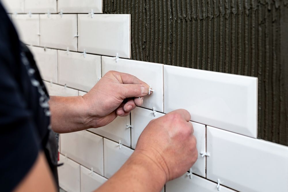Person installing white subway tile, using spacers.