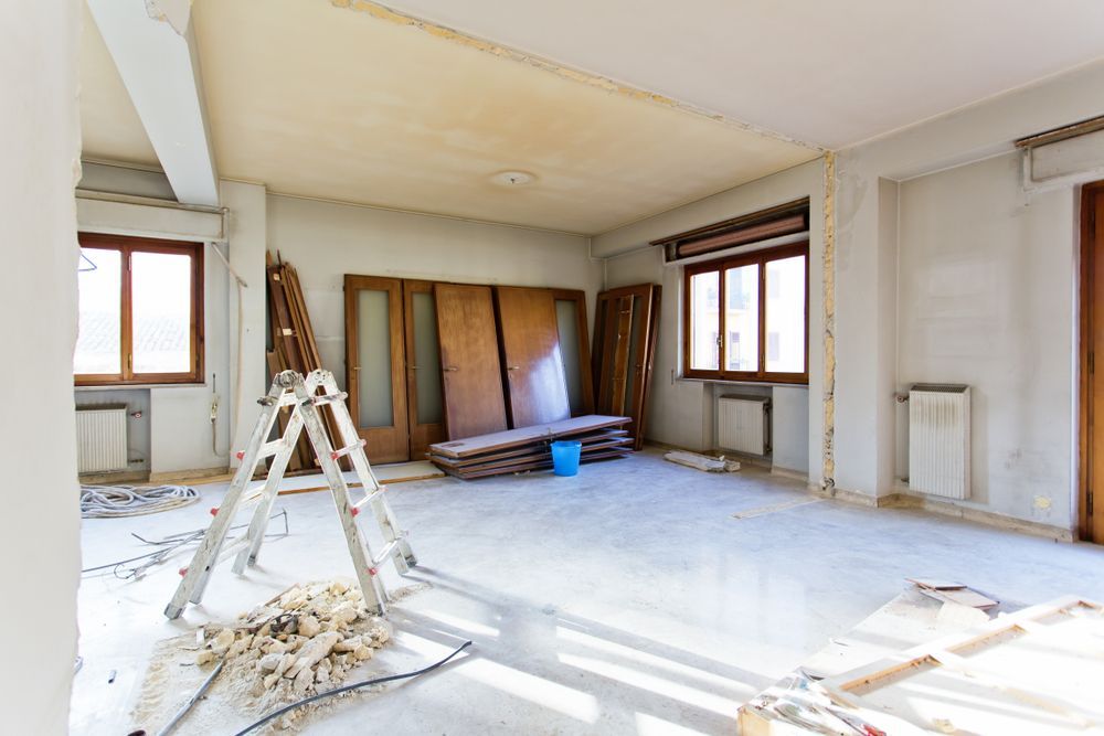 Room under renovation with a ladder, doors, and scattered debris; natural light streams in.