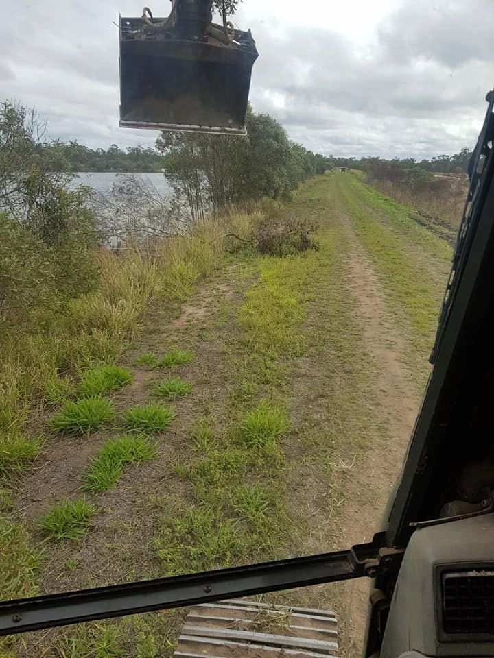 A Tractor is Driving Down a Dirt Road Next to a Lake — B E Laser Levelling QLD in Hervey Bay, QLD