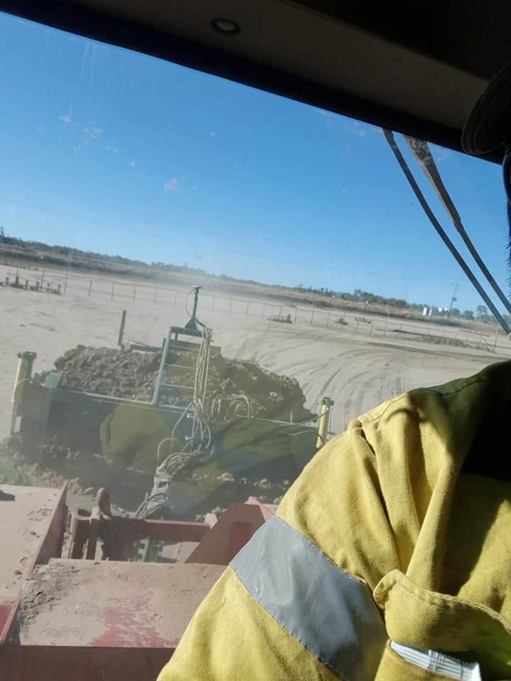 A Man in a Yellow Jacket is Driving a Bulldozer on a Dirt Road — B E Laser Levelling QLD in Bucca, QLD